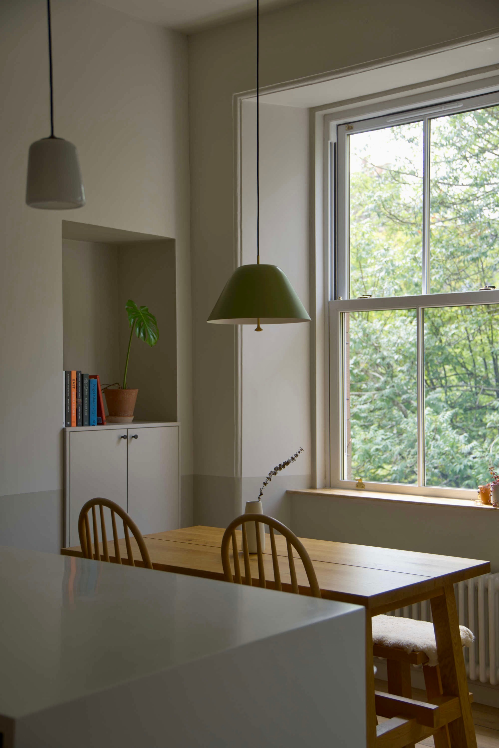 Dining area with wooden table and chairs, contemporary Edinburgh Press, green pendant light, and large sash window overlooking trees.