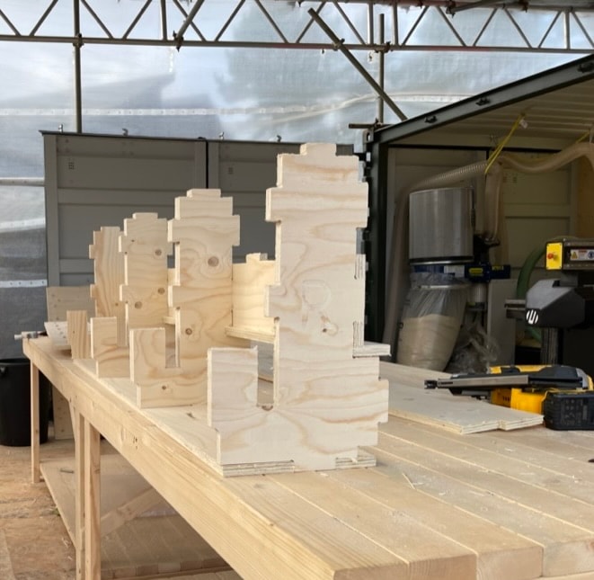 CNC-cut plywood pieces being assembled on a workbench with a CNC machine in the background.