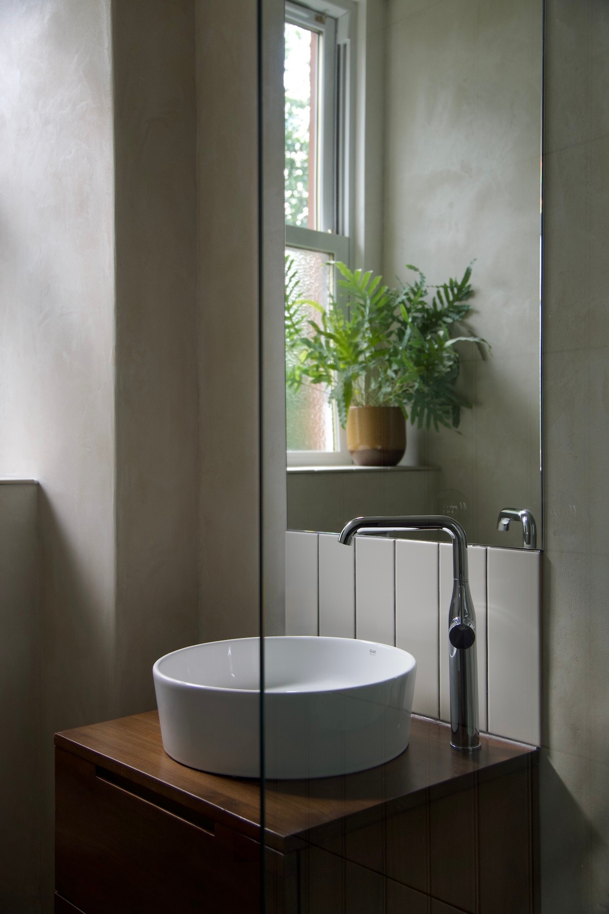Bathroom with light clay plaster walls, round basin on a walnut vanity unit, tiled splashback and tall mirror.