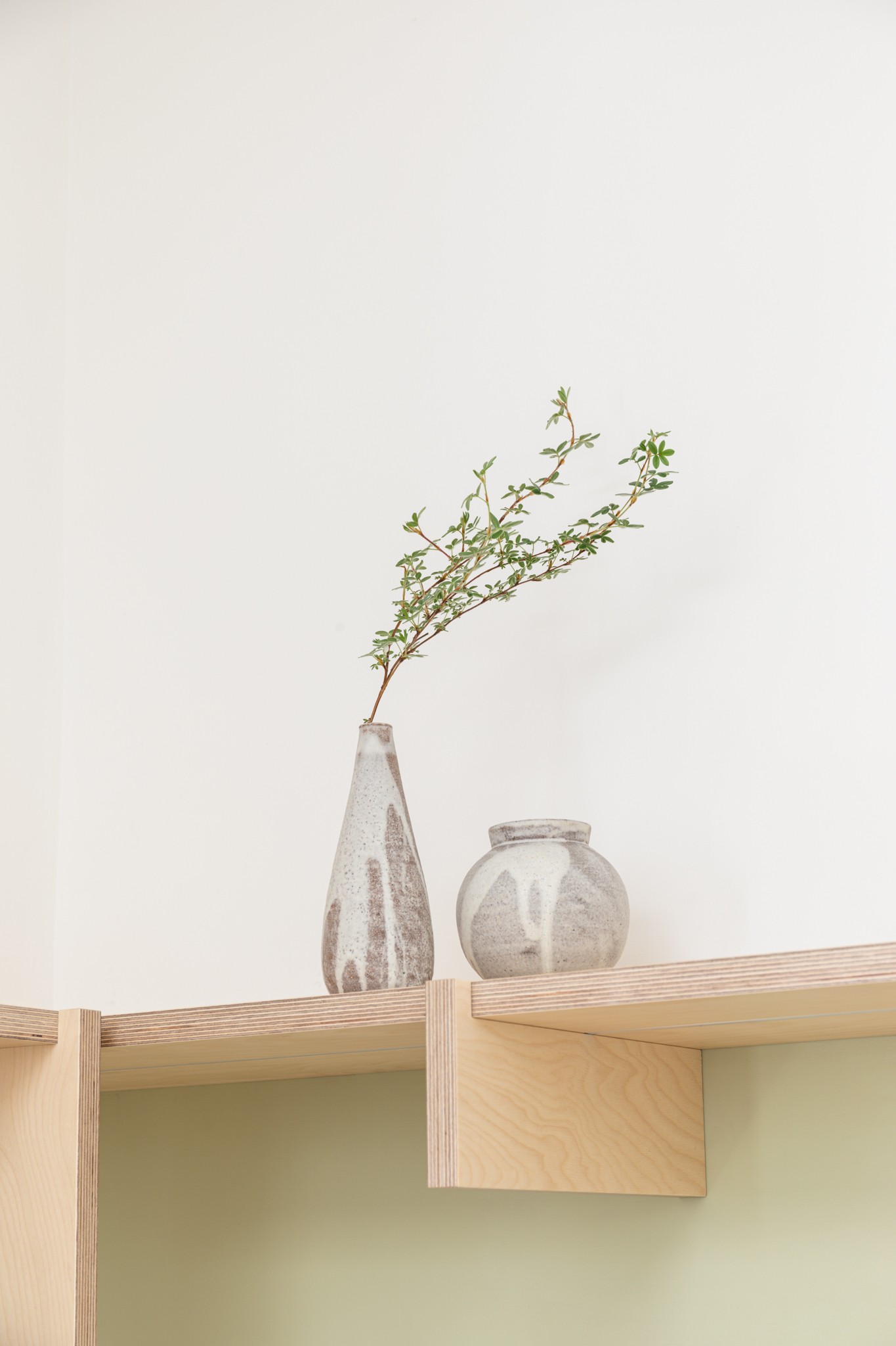 Two ceramic vases sat on a birch plywood shelf with integrated birch plywood bracket and a light sage green wall below.
